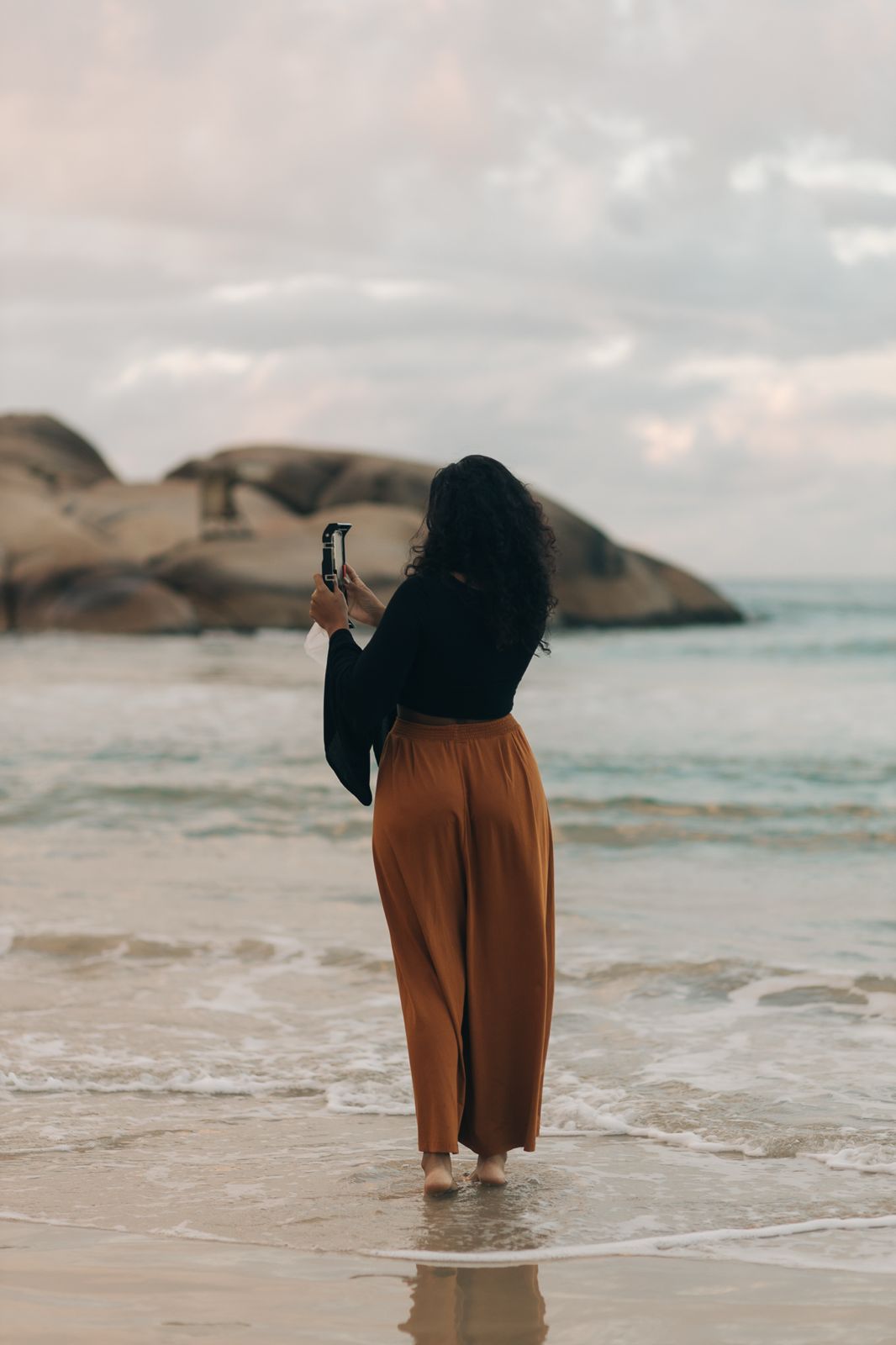 Valkiria Soares registrando uma história com o celular à beira-mar